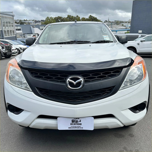 White mazda bt-50 pickup truck with black front grille and chrome emblem featuring monsoon and bonnet guard accessory