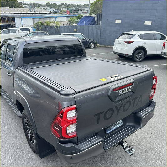 Dark gray toyota hilux pickup truck back side with ruggedized manual roller shutter tonneau cover matching the bed