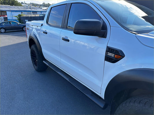 White ford ranger with black stainless steel 4 inch oval tube running board and rugged tires visible from the back