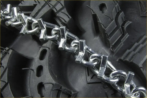 Shiny metallic v-bar tire chains with interlocking links wrapped around rugged black tire for suzuki quadsport z400