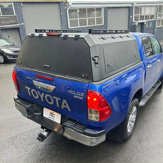 Blue toyota hilux sr5 pickup truck with black aluminium canopy and roof rack showing the back side view
