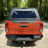 Back view of orange toyota hilux rugged x with black aluminium canopy and rear view glass 2015-2025 model