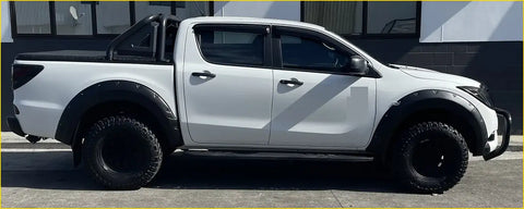 White mazda bt-50 pickup with black bolt flares rugged off-road tires and a protective roll bar