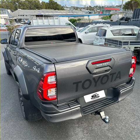 Dark gray metallic toyota hilux revo with electric roller shutter tonneau cover over truck bed from back side view