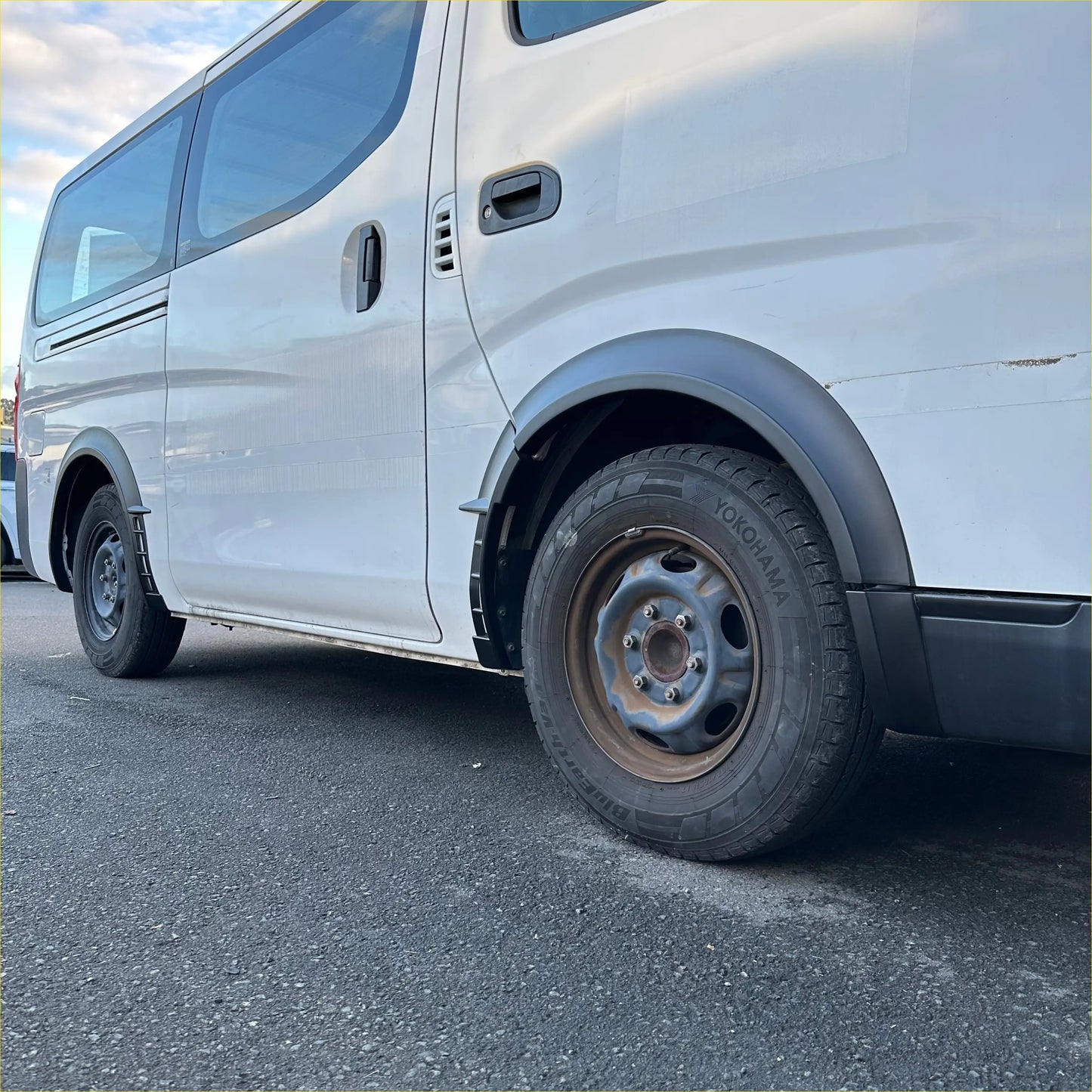 White nissan nv350 caravan with black matte sport style fender flare and yokohama tires front side view