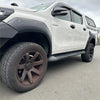 White toyota hilux rocco 2018-2020 with black lychee texture fender flares and roof rack from the back side