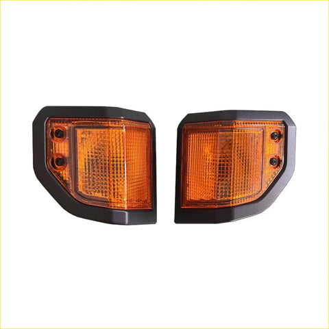 A pair of front corner indicator lights with black frames and amber textured lenses for vehicle signaling