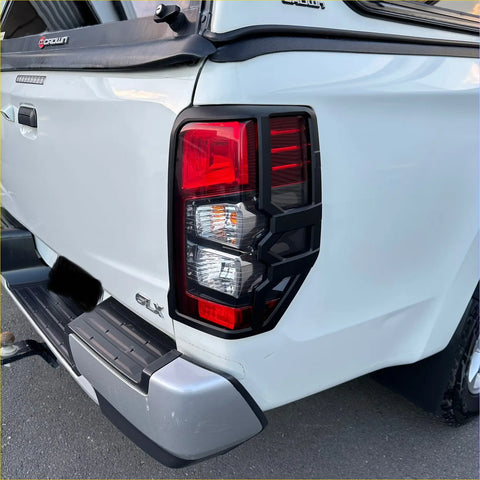 Black plastic taillight cover with red and clear lens sections shown from the back on a white mitsubishi triton 2019-2023 pickup truck