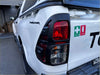 Back side of white toyota hilux 2025 sr with matte black headlight and taillight covers and black tailgate trim