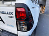 Back view of white toyota hilux 2025 sr with matte black headlight and taillight covers featuring black plastic trim