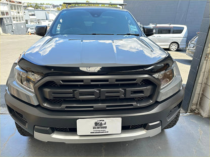 Black and silver ford ranger wildtrak with bold grille rugged tires and roof rack featuring monsoon and bonnet guard