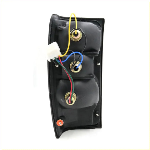 Back side of black plastic rear tail light assembly with three metal connectors and multicolored wiring for Toyota Hilux