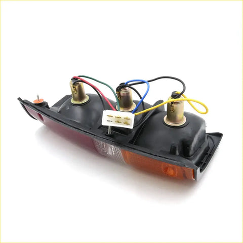 Back side of black plastic rear tail light left assembly with red amber lenses and wiring connector for toyota hilux 1984-1988