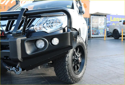 Black rugged rockarmor elite steel bullbar with fog lights and tow hook mounted on mitsubishi triton mq off-road vehicle