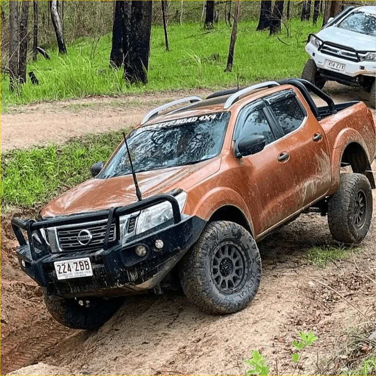 Orange nissan navara pickup with black off-road tires and a rugged rockarmor elite steel bullbar front bumper