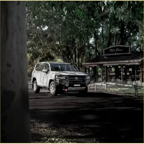 White toyota land cruiser 4wd with rockarmor gt hoop steel bullbar and offroad tires parked under leafy trees