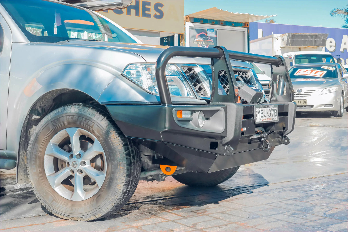 Black metal front bumper guard with integrated lights and tow hook on silver nissan navara d40 pickup truck