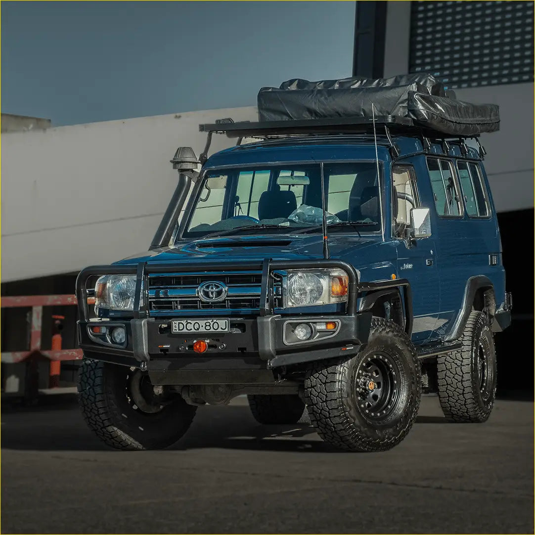 Blue toyota land cruiser 70 with black off-road tires and roof rack featuring rockarmor premium steel bullbar