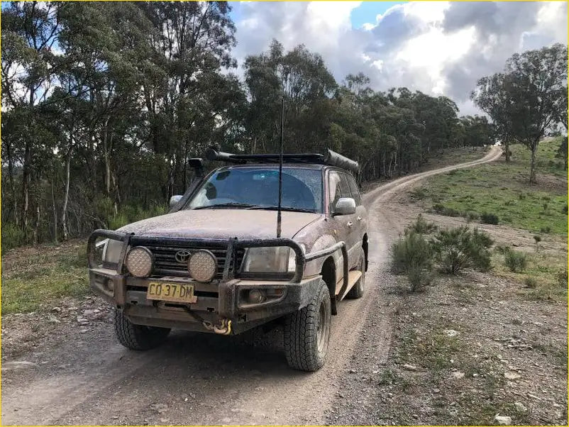 Mud-splattered brown toyota land cruiser with rugged rockarmor steel bullbar and roof rack for off-road use