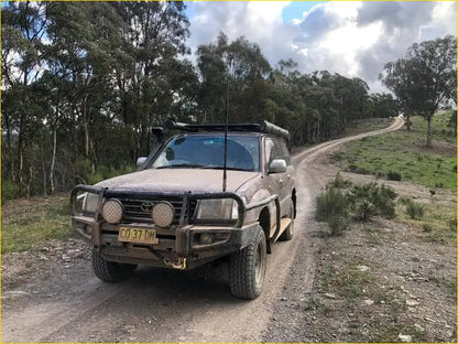 Mud-splattered brown toyota land cruiser with rugged rockarmor steel bullbar and roof rack for off-road use
