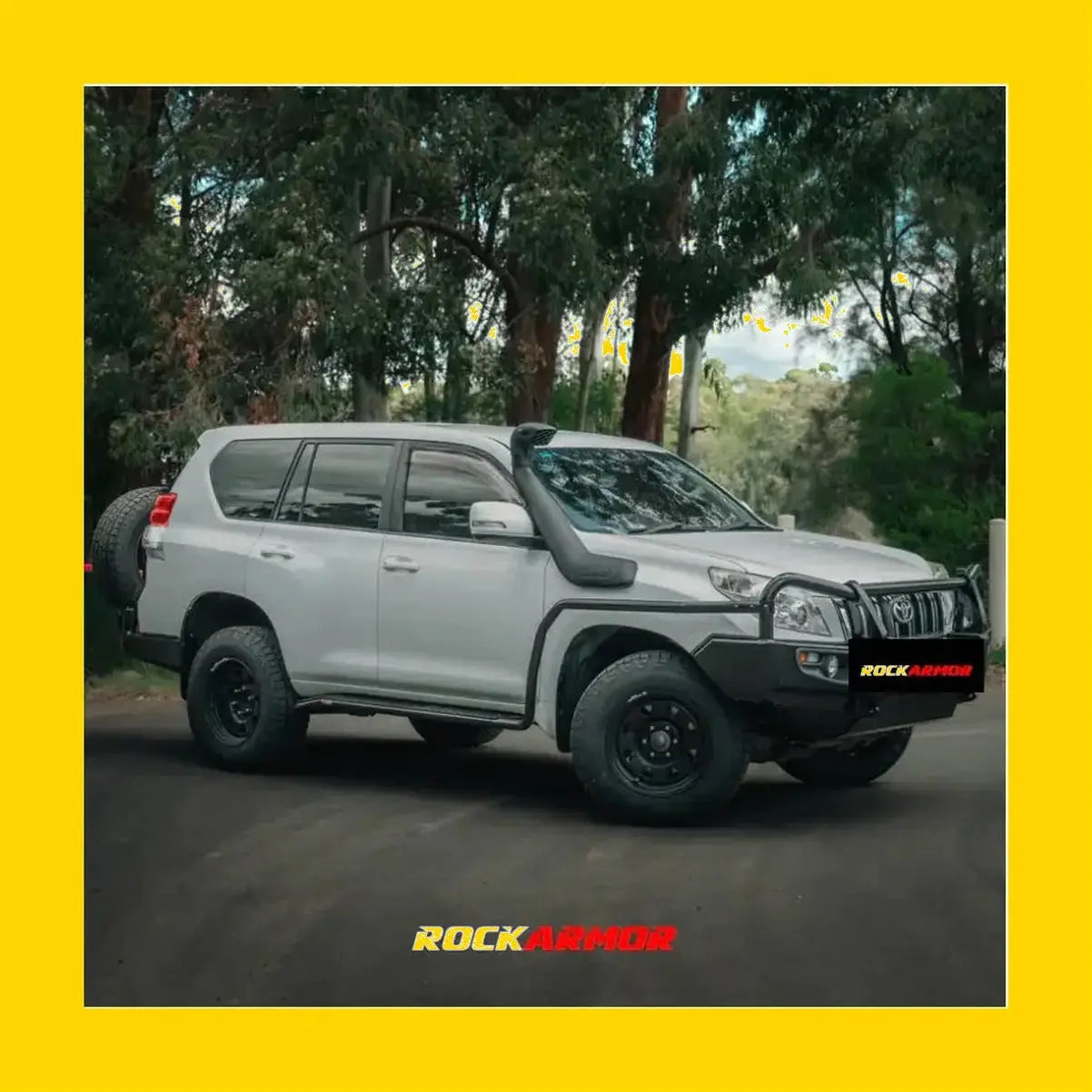Silver toyota land cruiser prado with black rockarmor rock sliders side steps and rear spare tire shown from back side