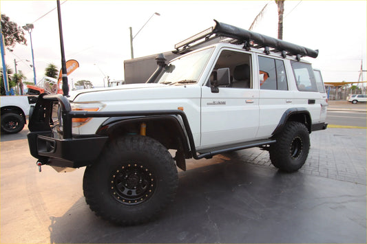 White toyota land cruiser 70 with black off-road wheels showing rockarmor steel rockslider side steps from the back side