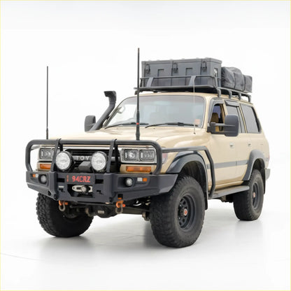 Beige toyota land cruiser with black rockarmr premium steel bullbar roof rack carrying gray storage box and bag