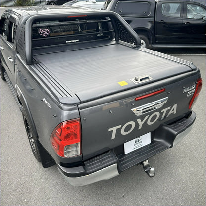 Dark gray toyota hilux with black manual roller shutter and chrome roll bar t10 shown from the back side
