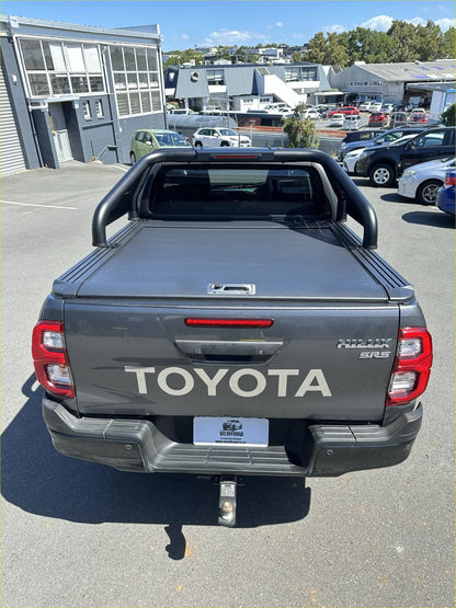 Back view of dark gray toyota hilux sr5 with black tubular roll bar and manual roller shutter tonneau cover