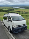 White toyota hiace van with black heavy duty roof rack and dark gray bumper showing the front side