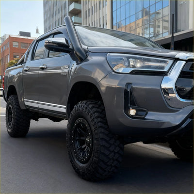 Gray metallic toyota hilux revo 2015 with black stainless steel snorkel and off-road tires shown from the back side