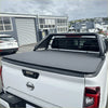 Black soft tonneau cover fitted over the bed of a white nissan navara pickup truck from the back side