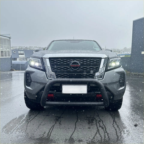 Silver nissan navara pickup with stainless steel black nudge bar and illuminated headlights front view