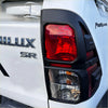 Back side of matte black taillight cover with red clear lens on white mitsubishi triton pickup truck