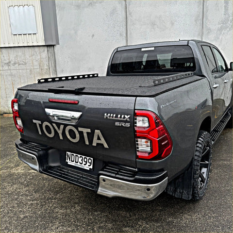 Dark gray toyota hilux sr5 double cab with black tomahawk aluminium hardlid and off-road tires shown from the back side